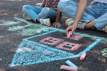 Little child and her mother drawing with colorful chalks on asphalt, closeup
