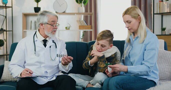 Accelerating shooting of likable confident caring senior bearded family doctor which visiting at home his sick boy patient and giving medicines to boy's mother for treatment