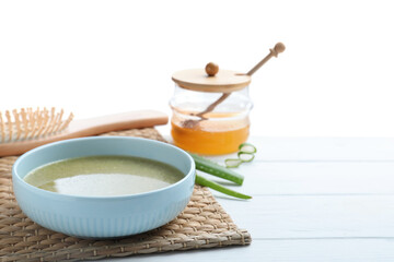 Homemade hair mask in bowl, fresh ingredients and brush on wooden table against white background. Space for text