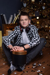 Attractive guy teenager sitting on the floor of the christmas living room and holding a box with a gift