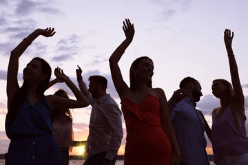 Group of friends having fun near river at sunset. Summer party