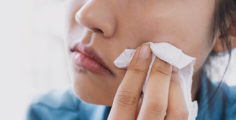 A woman is using tissue paper to wipe her face.