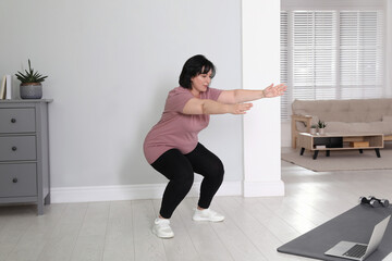 Overweight mature woman squatting while watching online class at home