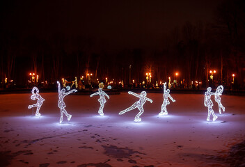 Glowing christmas street decorations. Decorative figure skaters from white lamps and wire garland. New Year in night park
