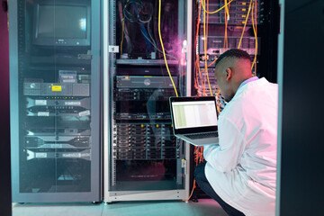 African american male computer technician using laptop working in business server room