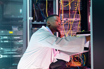 African american male computer technician using laptop working in business server room