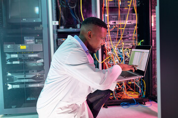 African american male computer technician using laptop working in business server room