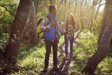 Happy diverse couple with backpacks hiking in countryside