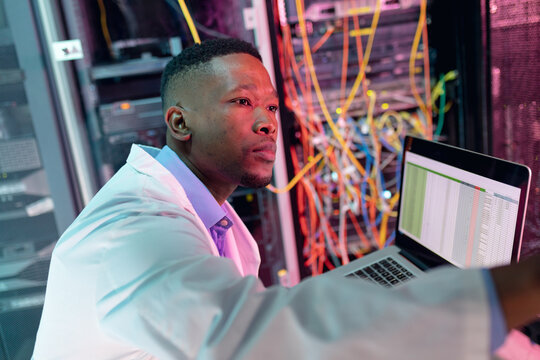 African american male computer technician using laptop working in business server room