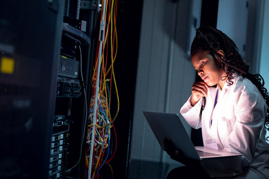African american female computer technician making call and using laptop working in server room