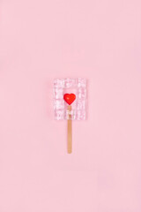 Ice cream with ice cubeas and red hearth in the middle on the pink background.Valentines day creative compostion. Minimal composition.