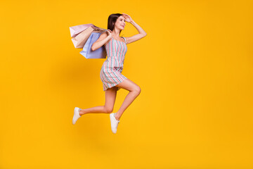 Full length body size woman smiling jumping running on sale with bags looking far isolated vivid yellow color background