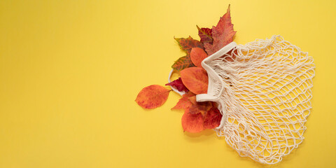 autumn leaves in eco mesh bag on bright yellow background.