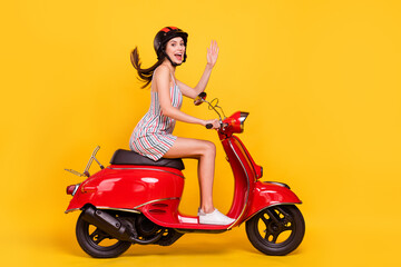 Obraz na płótnie Canvas Full length body size side photo woman riding bike wearing dress helmet waving hand greeting isolated bright yellow color background