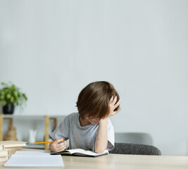 Child sitting at the desk, exhausted from homework and learning. Problems with school examinations and activities,educational difficulties in youngsters. In preschool lot of work and drained stress.