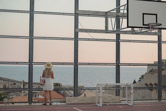 Young traveler girl play basketball inside the fortress with sea on the background. Popular tourist destination, tourists take pictures of medieval fortification. Gorgeous stone building in Dubrovnik