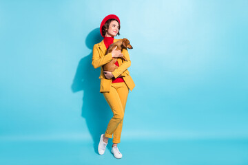 Photo of sweet adorable young woman dressed red headwear holding dog looking empty space smiling isolated blue color background