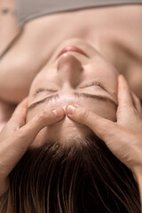 Young beautiful woman is getting a relaxing head and face massage in wellness center. Masseur doing massage the head of an young beautiful girl woman in the spa salon close up macro