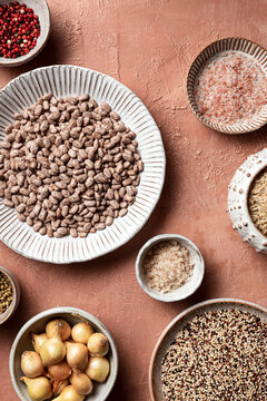 An overhead view of a variety of pantry staples, including beans, quinoa, and spices, shot on a terra cotta background