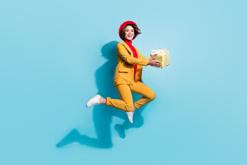 Fototapeta na wymiar Photo of cute funky young lady wear yellow blazer red cap smiling holding gift box isolated blue color background