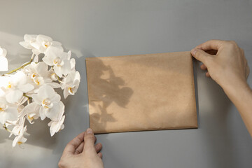 Hands holding an empty brown craft envelope of A5 format on a gray background. Top view of the...
