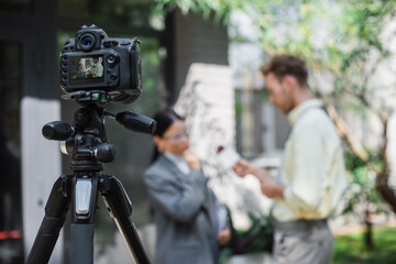 digital camera with reporter holding microphone while taking interview of asian businesswoman in glasses on screen