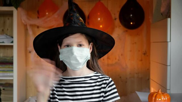 4k. Halloween kids mask. Teen girl in witch costume and black hat. Child puts on protective medical face mask and getting ready to celebration. Halloween. Protecting from COVID-19.