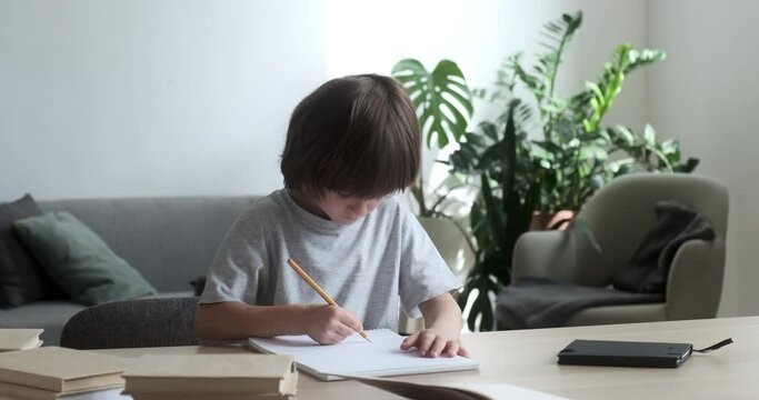 Cute preschooler boy learning writing and doing homework and exercises at home. An elementary school kid pupil is getting ready to go to class and is drawing with a pencil.