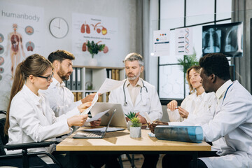 Caucasian female doctor using wheelchair sitting with multiracial colleagues at bright office and discussion progress in medicine. Practitioners sharing with knowledge and ideas during conference.