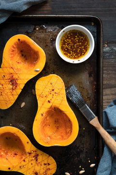 Butternut pumpkin halves basted with chilli oil on a baking tray.