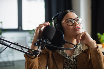 Fototapeta na wymiar asian radio host in glasses and headphones looking up while talking in broadcast studio