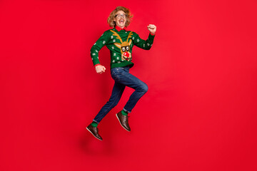 Photo of handsome funky young man wear green sweater spectacles smiling jumping running isolated red color background