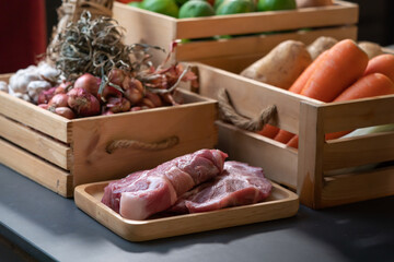 raw Pork is laid in front of vegetable, potato, carrot, shallot, lime, onion, tomato that in wood box. With studio light environment.