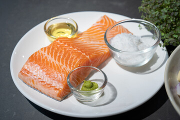 Salmon steak, Raw fillet of sea fish salmon or trout on white dish with salt, oil, and wasabi cream in studio light on dark background.