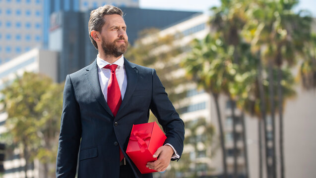 successful businessman in suit hold present box standing outdoor, anniversary