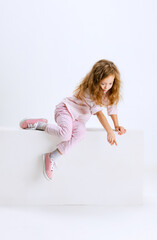 Studio shot of cute beautiful girl with long silk hair in casual clothes sitting on big box isolated on white background.