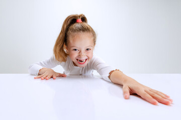 Portrait of beuatiful school girl sitting and looking at camera isolated on white background. Happy childhood, education