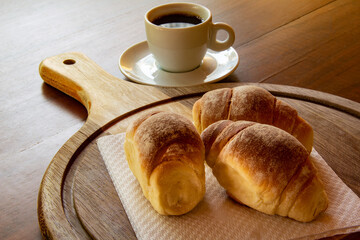 Três pães caseiros sobre uma tábua e uma xícara de café preto. Café da manhã.