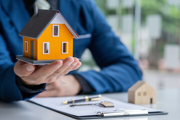 Real estate agent passing house model to his client, Hand of real estate agent passes the key to...