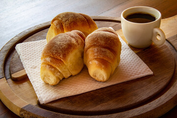 Três pães caseiros sobre uma tábua e uma xícara de café preto. Café da manhã.