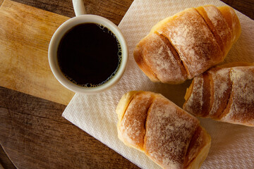 Três pães caseiros sobre uma tábua e uma xícara de café preto. Café da manhã.