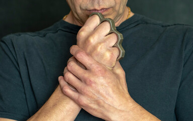 Portrait of a 45-50-year-old man with brass knuckles in his hand on a dark background, close-up, selective focus. Concept: attack of robbers, street gangs, self-defense from hooligans.