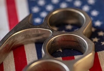 Metal brass knuckles lying on the background of the American flag, close-up, selective focus. Concept: prohibited and permitted use of cold weapons, crime in America, criminal showdowns.