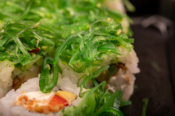 Delicious sushi roll with Philadelphia cheese, cucumber, salmon and chuka in a plastic tray on a wooden table.