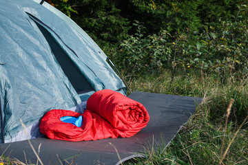 Red sleeping bag near camping tent on green grass outdoors, space for text