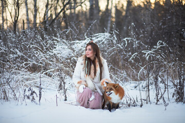 A beautiful girl walks with a fox in a snowy forest. Cold weather. Winter's Tale. Red fox....