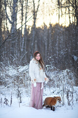 A beautiful girl walks with a fox in a snowy forest. Cold weather. Winter's Tale. Red fox. Photoshoot in a fairy-tale style.