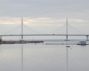 Large elegant cable-stayed bridge with different cars. Reflection of the cable-stayed bridge in calm water.