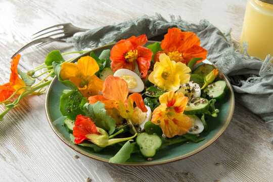 plate with salad of cucumbers, eggs and edible nasturtium flowers on a wooden table