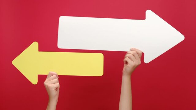 Close up of female hands hold two paper arrow pointing left and right, isolated on red color background studio with copy space for your text or design. Business vision, choice, achievement concept